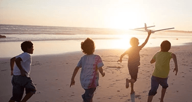four children running with a toy airplane on a beach