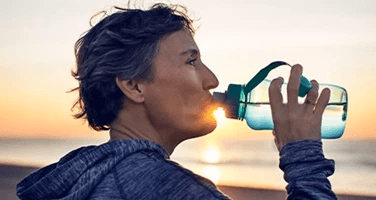 a lady drinking water on a beach at sunrise