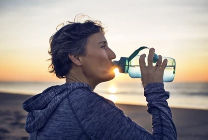 a lady drinking water on a beach at sunrise