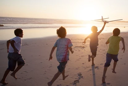 four children running with a toy airplane on a beach