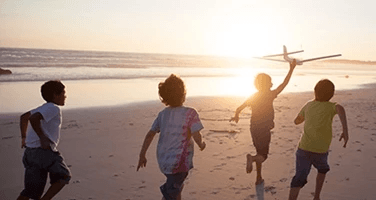 four children running with a toy airplane on a beach